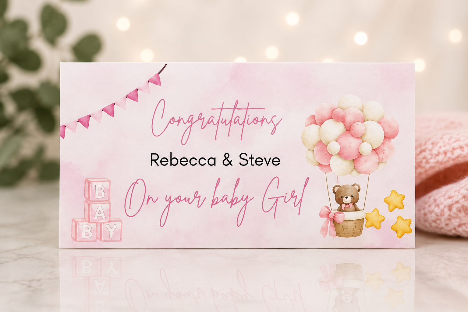 A personalized baby shower congratulations card with a pink watercolor background, featuring the text 'Congratulations Rebecca & Steve On your baby Girl' along with illustrations of pink and white balloons, a teddy bear, yellow stars, and pink baby blocks.
