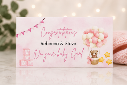 A personalized baby shower congratulations card with a pink watercolor background, featuring the text 'Congratulations Rebecca & Steve On your baby Girl' along with illustrations of pink and white balloons, a teddy bear, yellow stars, and pink baby blocks.